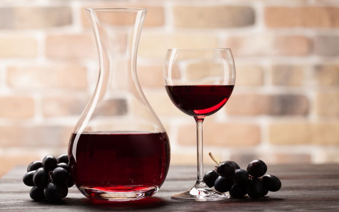 red wine in a wine glass and decanter next to grapes on table