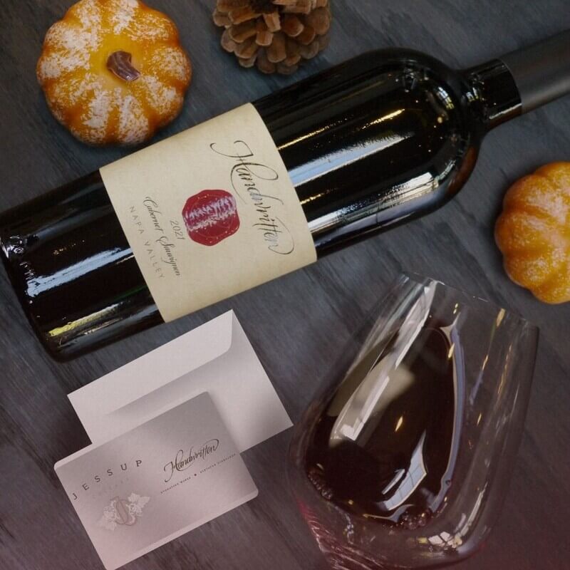 shot from above, table with wine glass, wine bottle, envelope with handrwitten and jessup gift card, and small pumpkins